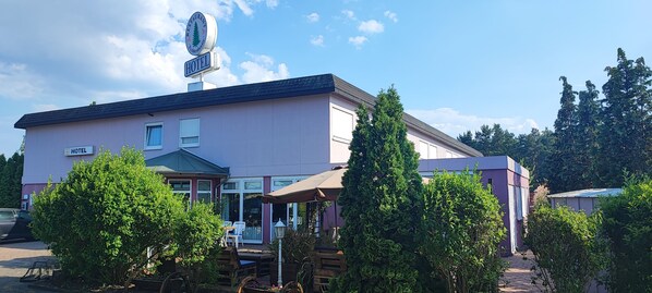 A hotel with a sign indicating a restaurant on the roof, a covered outdoor seating area, and a pathway leading to the entrance.
