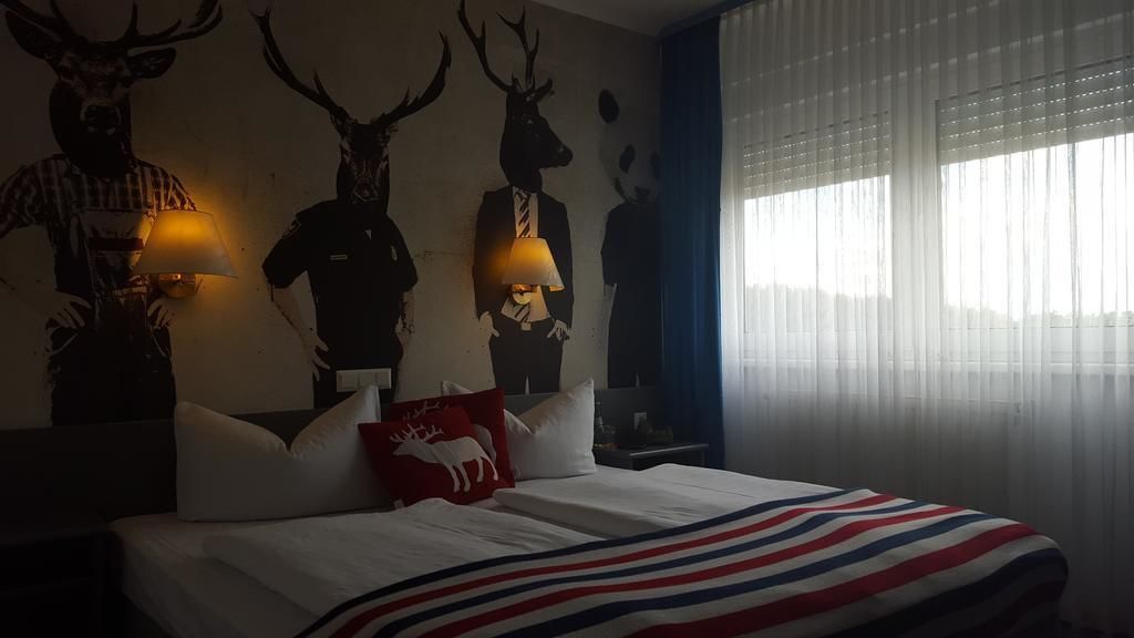 Una habitación de hotel con cama, lámpara, ventana con cortinas y adornos en la pared.
