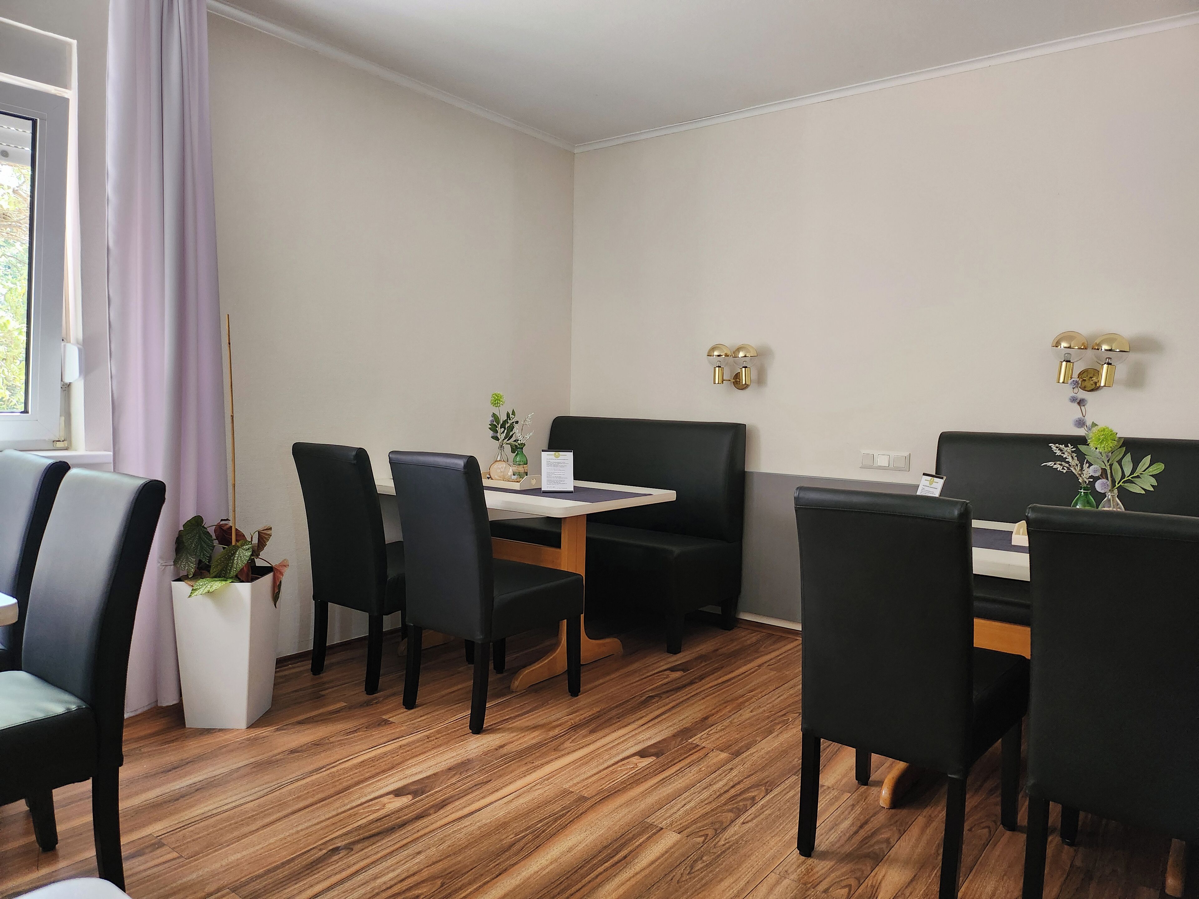 Een moderne eetruimte met een houten vloer, zwarte beklede stoelen, een witte tafel en een zwarte bank.