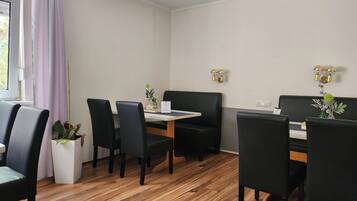 Een moderne eetruimte met een houten vloer, zwarte beklede stoelen, een witte tafel en een zwarte bank.