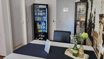 A hotel room with a minibar, a desk with a menu, a chair, and a wall with a cityscape mural.