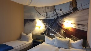 Quarto de hotel com duas camas, um grande mural de um navio na parede e duas luminárias fixadas na parede.