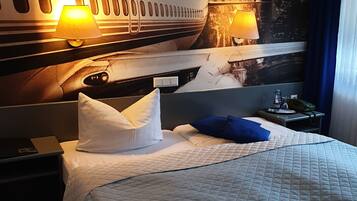 A hotel room with a bed, pillows, a nightstand, a lamp, and a wall mural of an airplane.