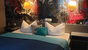 Una habitación de hotel con una cama, almohadas, una mesita de noche y una pared con grafitis y texto.