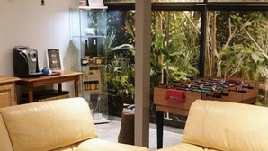 Ein Wohnzimmer mit einem gelben Ledersofa, einem Kicker und einer Vitrine mit diversen Gegenständen.