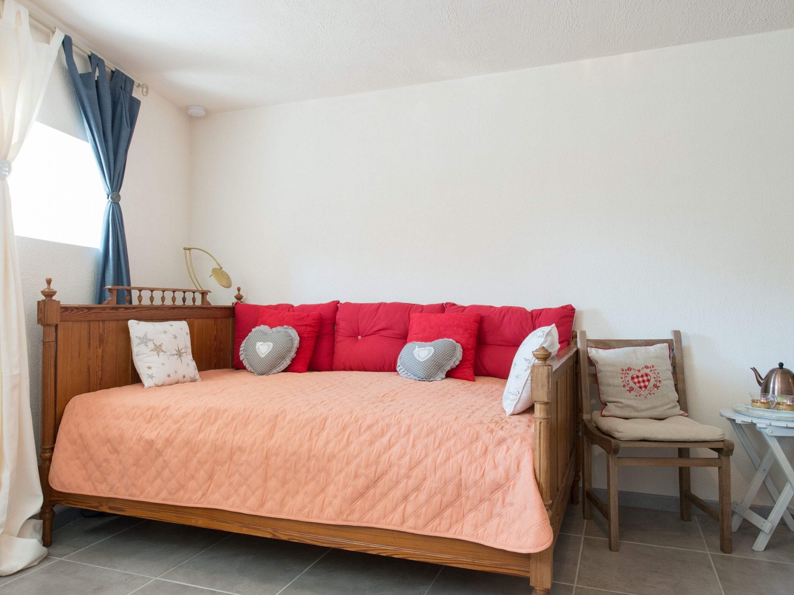 Une chambre à coucher avec un lit en bois, des oreillers rouges et une couvre-lit matelassée de couleur pêche.