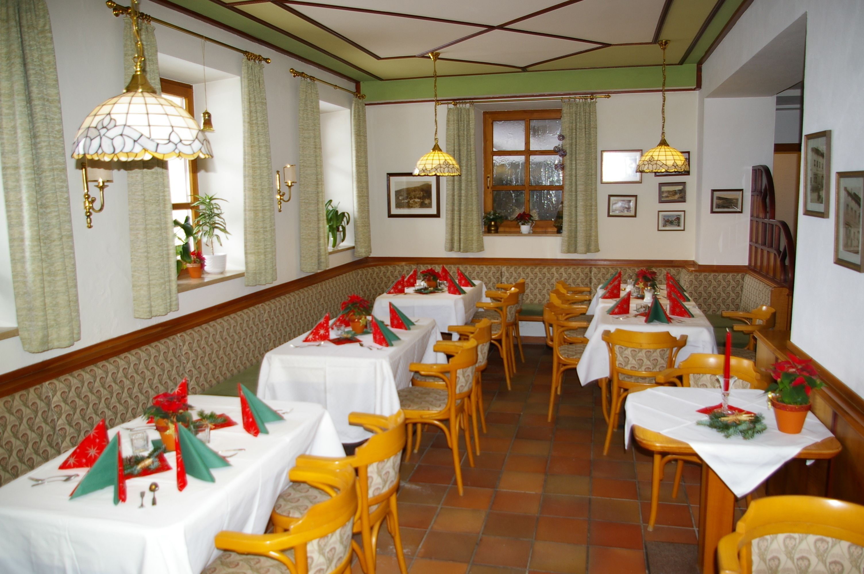 A dining area with multiple tables set for a meal, chairs, and hanging lamps.