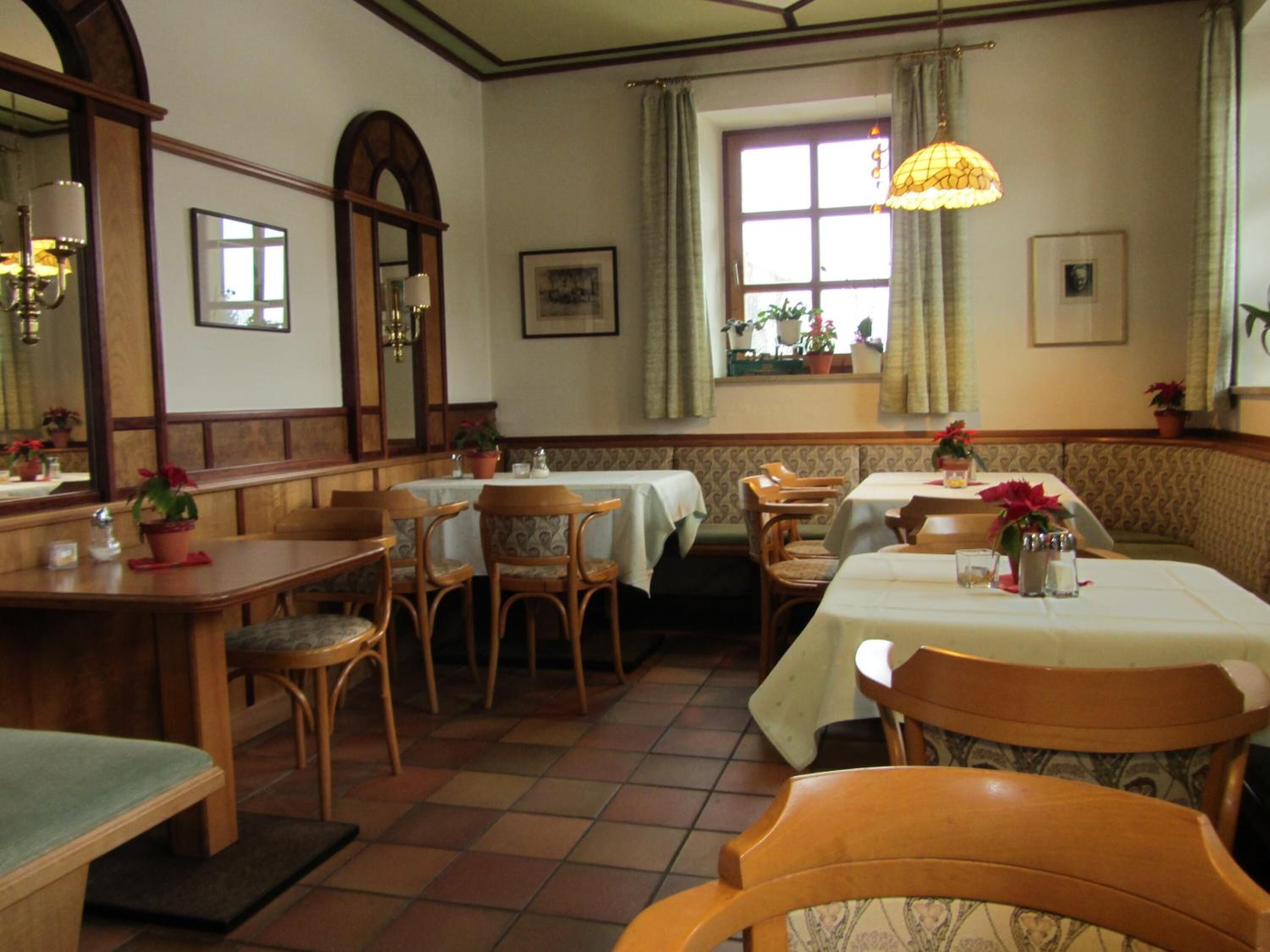 A cozy restaurant with wooden furniture, a tiled floor, and a window with curtains.