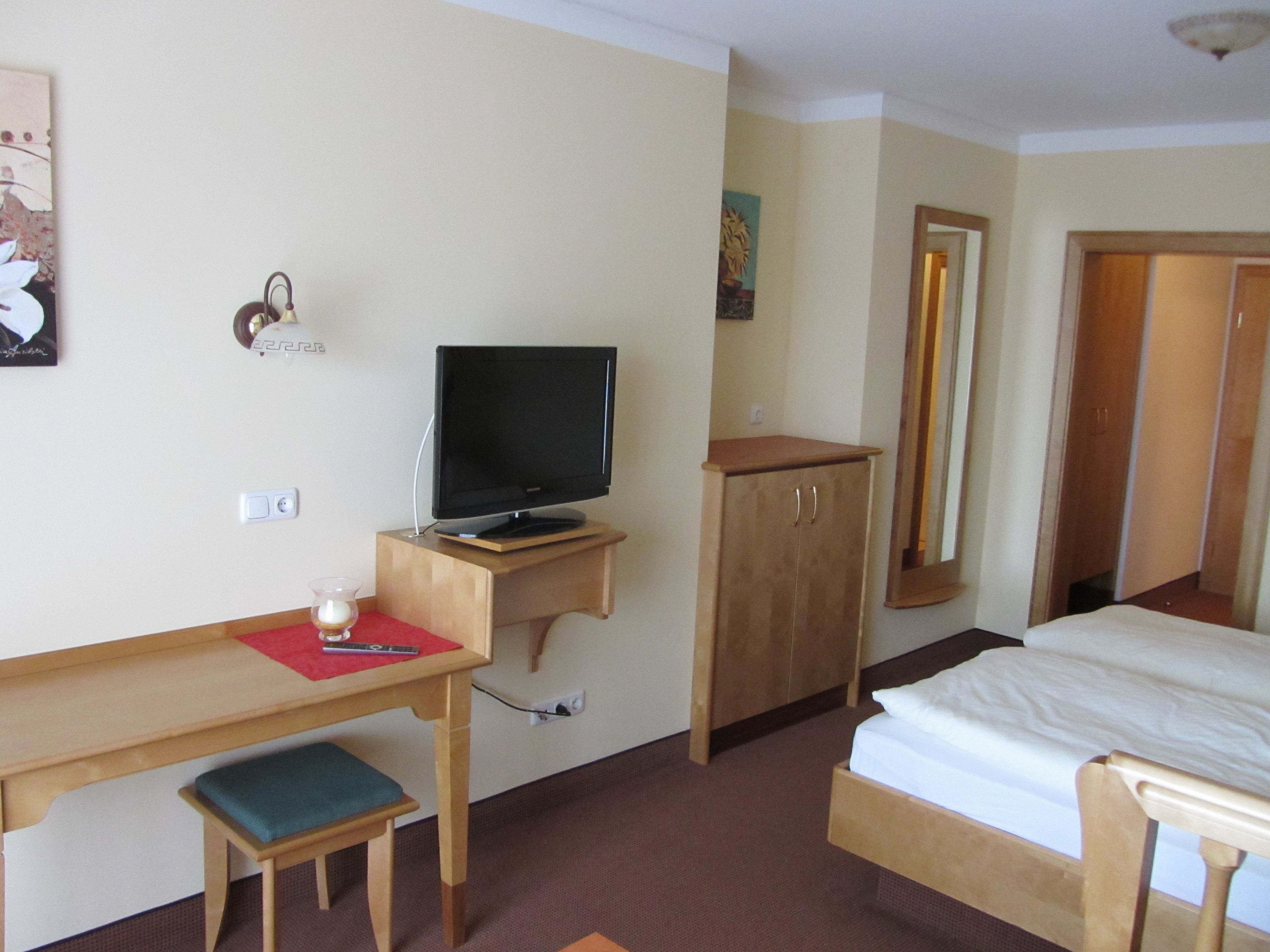 Une chambre d’hôtel avec un bureau en bois, une télévision, un lit et un miroir.