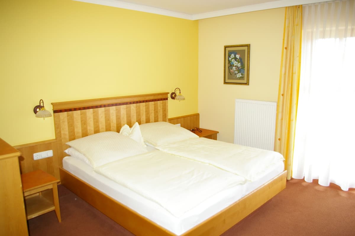 Ein Zimmer mit einem Einzelbett, einem Holz-Kopfstück, zwei Nachttischen, einem Nachtlicht und einer Heizung.