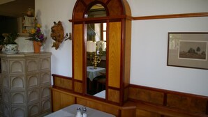 A room with a wooden bench, a small table with salt and pepper shakers, a mirror with a wooden frame, and a framed picture on the wall. - Pension Zur Alten Schmiede (Zwiesel)