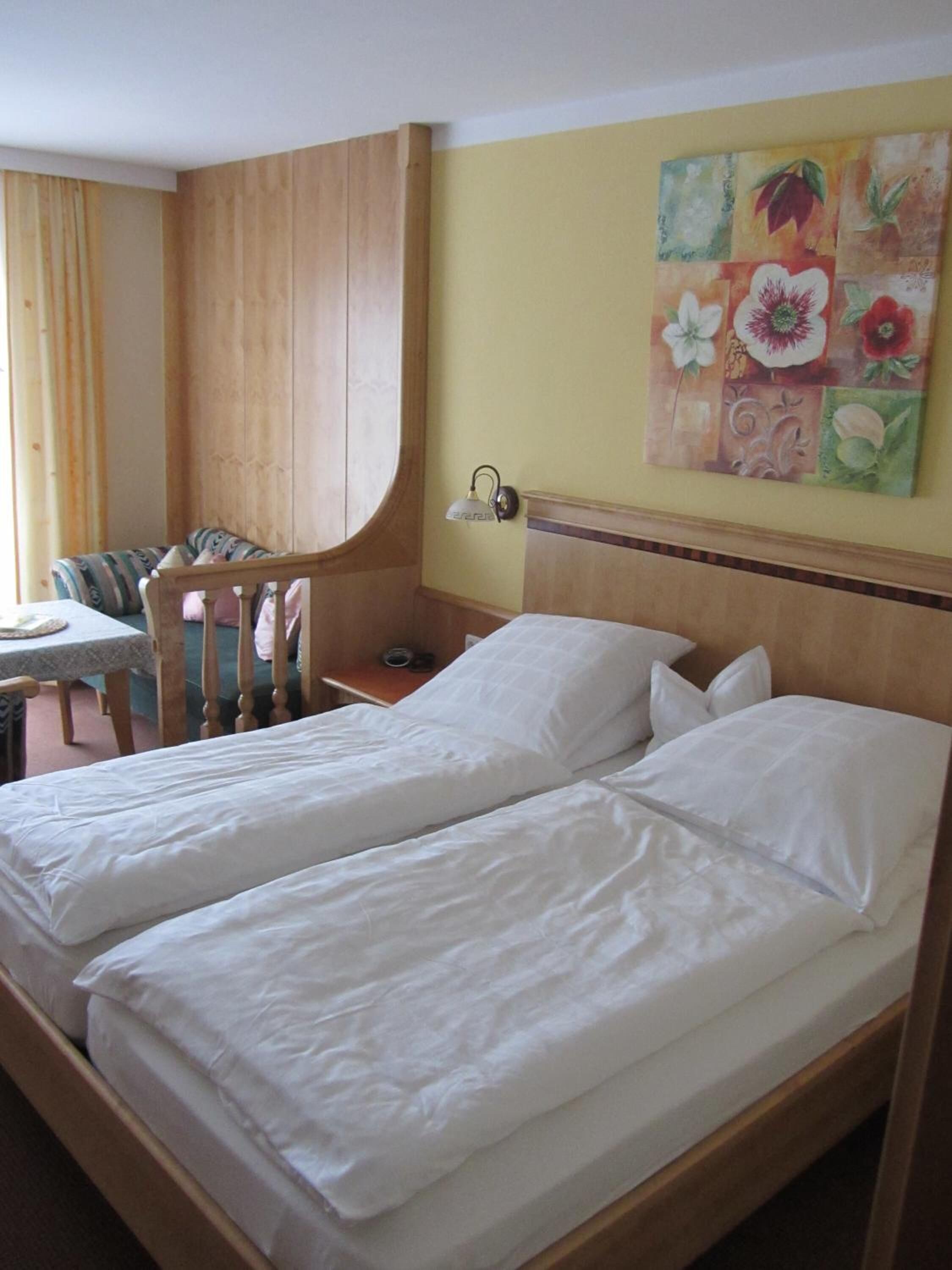 A room with two single beds, a wooden headboard, a small table with a chair, and a wall-mounted lamp.