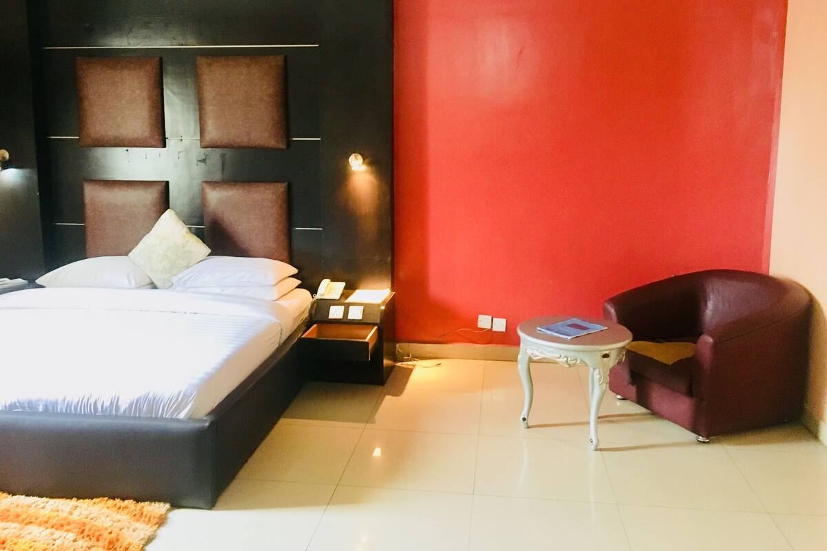 Une chambre d’hôtel avec un grand lit, une table de chevet, un mur d’accent rouge et une petite table avec une chaise.