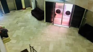 A spacious lobby with a tiled floor, a dark-colored sofa, and a glass door leading to another room.