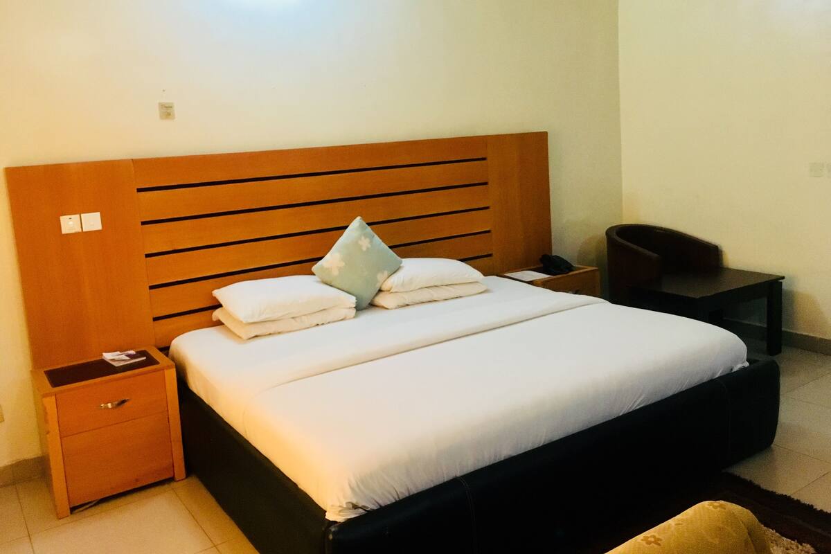 Un lit bien fait, avec une tête de lit en bois, une table de chevet avec une lampe et une petite poubelle.