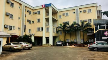 A hotel with a central entrance, multiple floors, and a parking area with several cars.