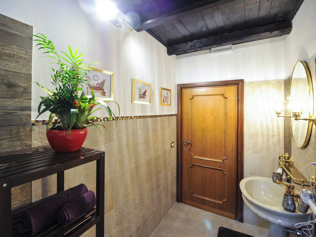 Un bagno con una porta in legno, un lavabo con accessori dorati, uno specchio e una pianta su un tavolo.