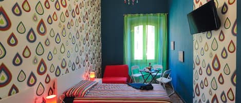 Quarto com uma cama, uma cadeira vermelha, uma mesa e uma televisão na parede.