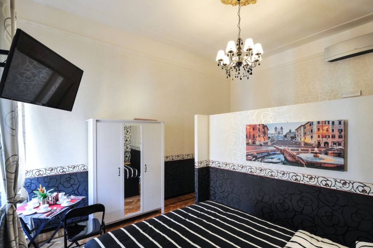 A hotel room with a bed, a desk, a chair, a wardrobe, and a chandelier.