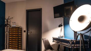 Habitación de hotel con una cama, un escritorio con silla, un televisor, una lámpara y una luz de aro.