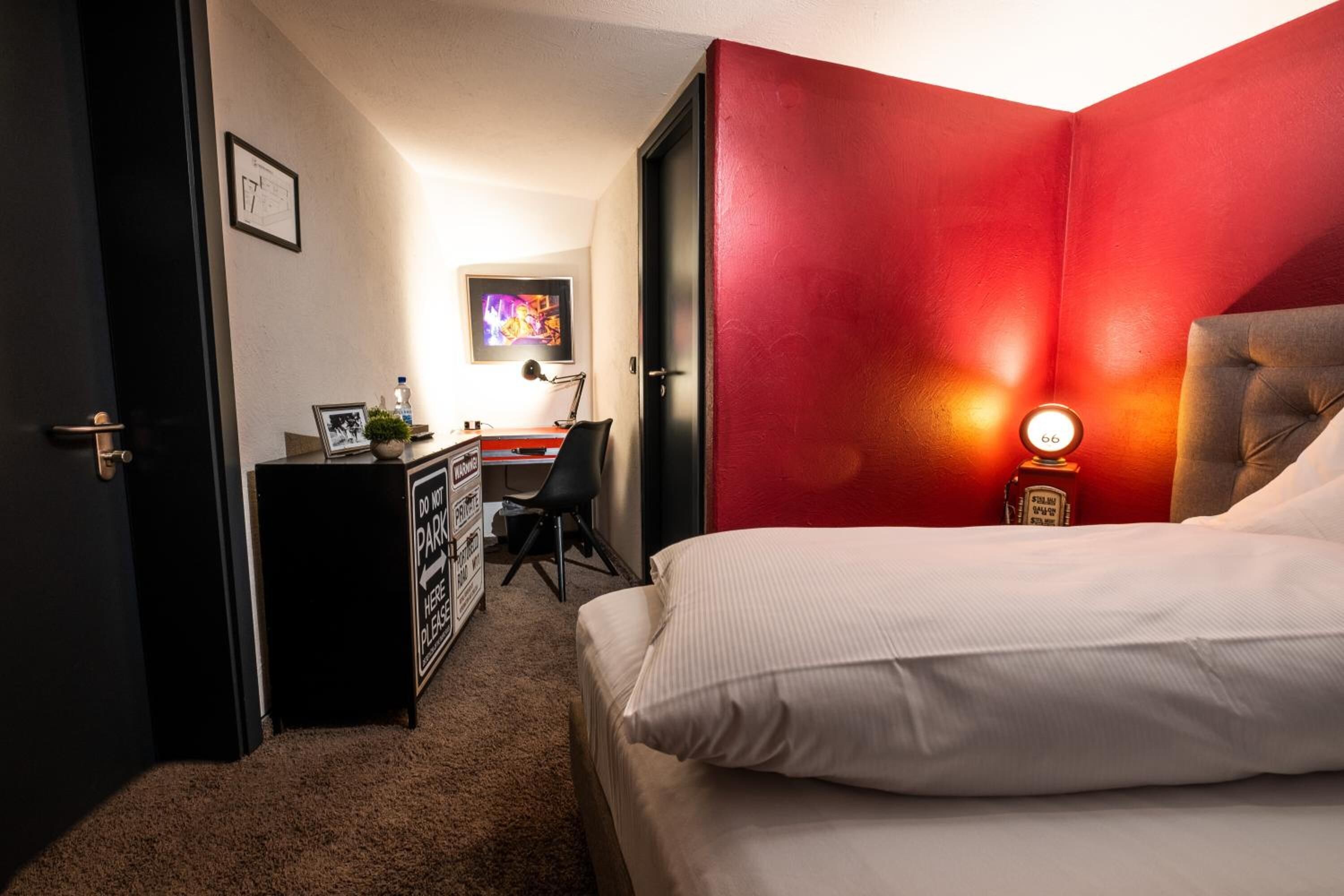 Ein Schlafzimmer mit einem Bett, einem Schreibtisch, einem Sessel und einer roten Akzentwand.