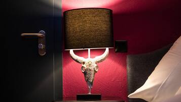 A room with a red wall, a bull's head sculpture, a lamp, a bed, and a door.