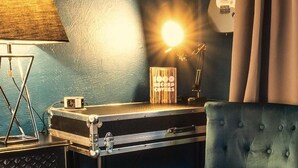 Une pièce avec un mur bleu, un tableau encadré représentant un groupe de musique, une guitare électrique blanche, une lampe et un fauteuil bleu.