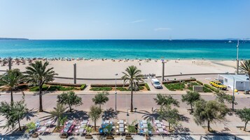Una playa con un paseo pavimentado, palmeras y zonas de estar al aire libre.