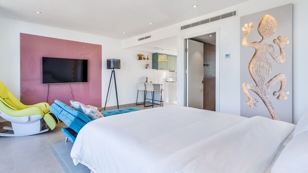 Una habitación de hotel moderna con una cama grande, un televisor, un escritorio y una obra de arte original en la pared.