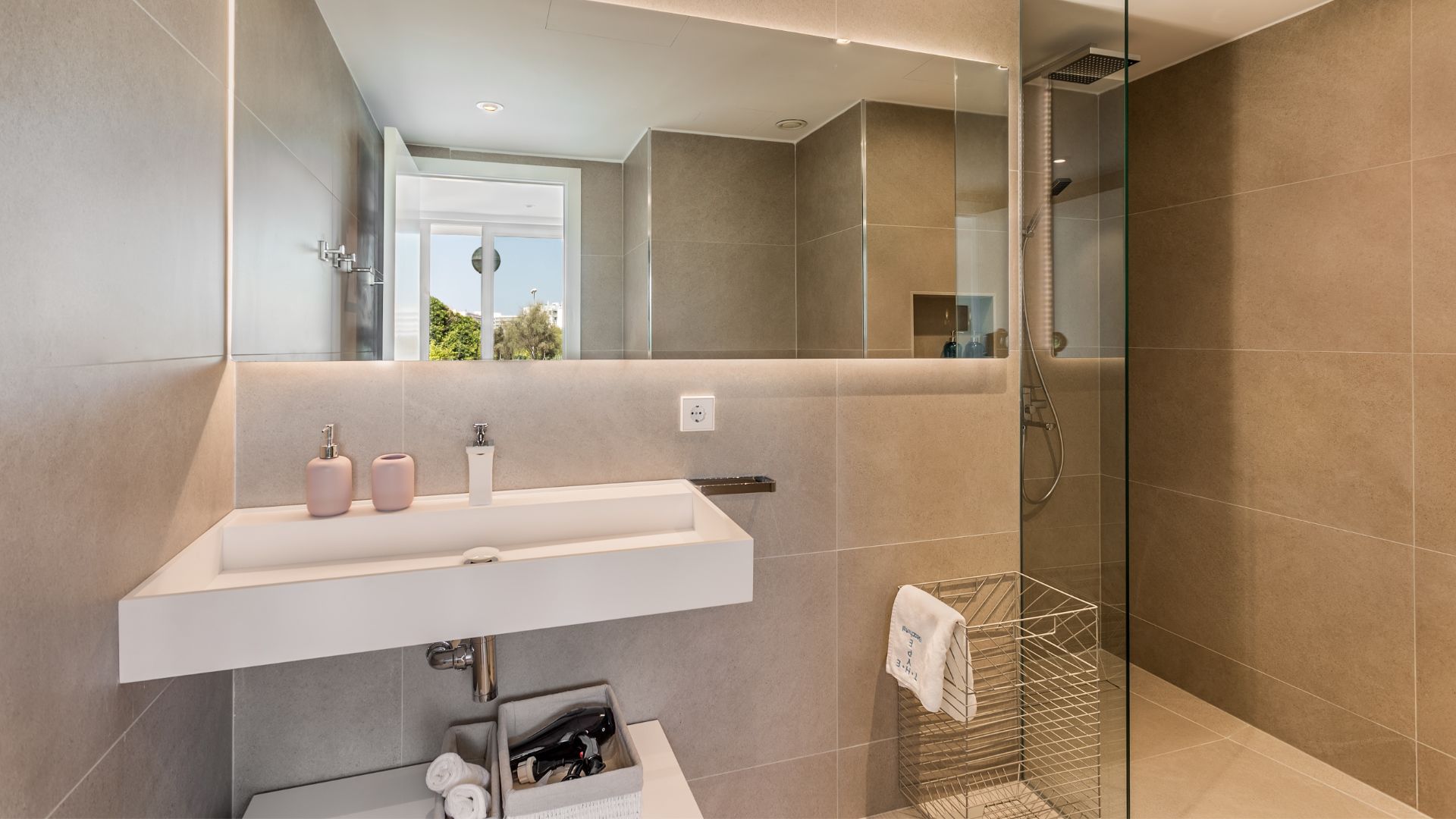 Een moderne badkamer met een grote spiegel, een witte wastafel en een douche met glazen wanden.