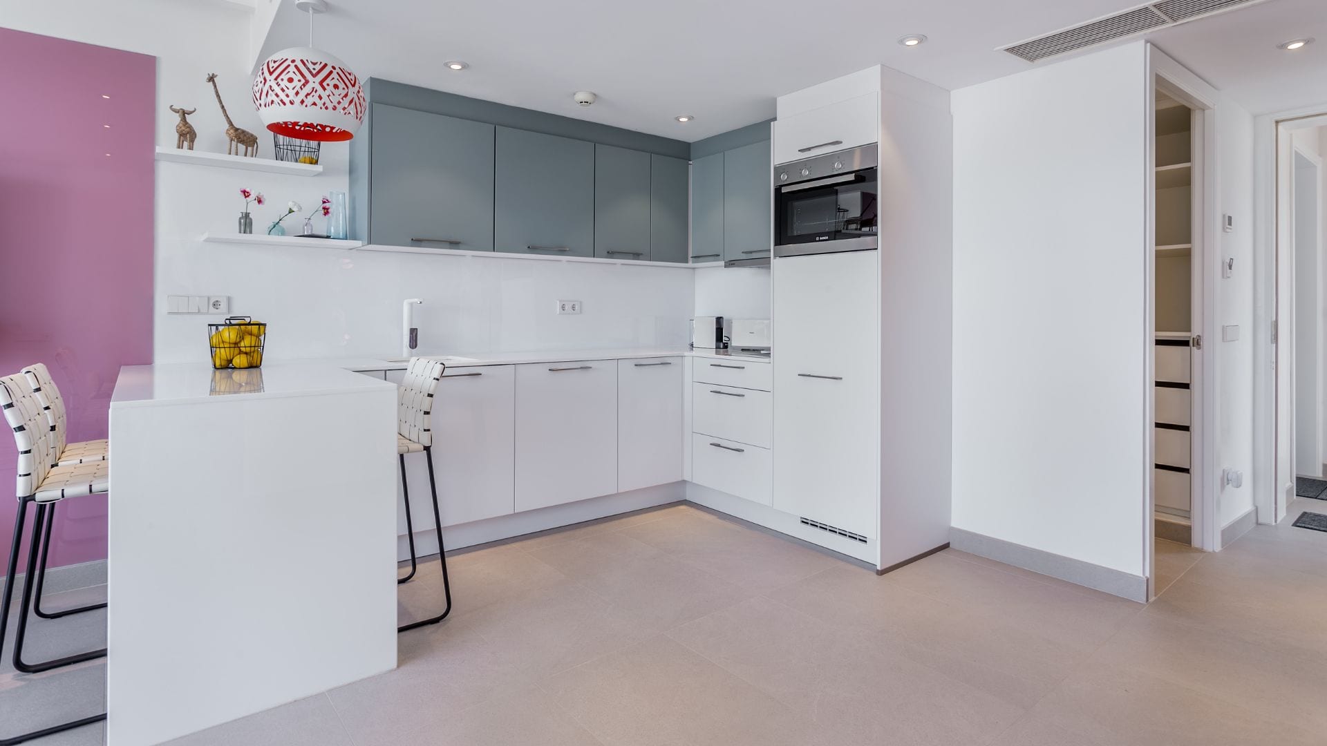 Une cuisine moderne avec des armoires blanches, un four encastré et un coin repas comprenant une table et des chaises blanches.