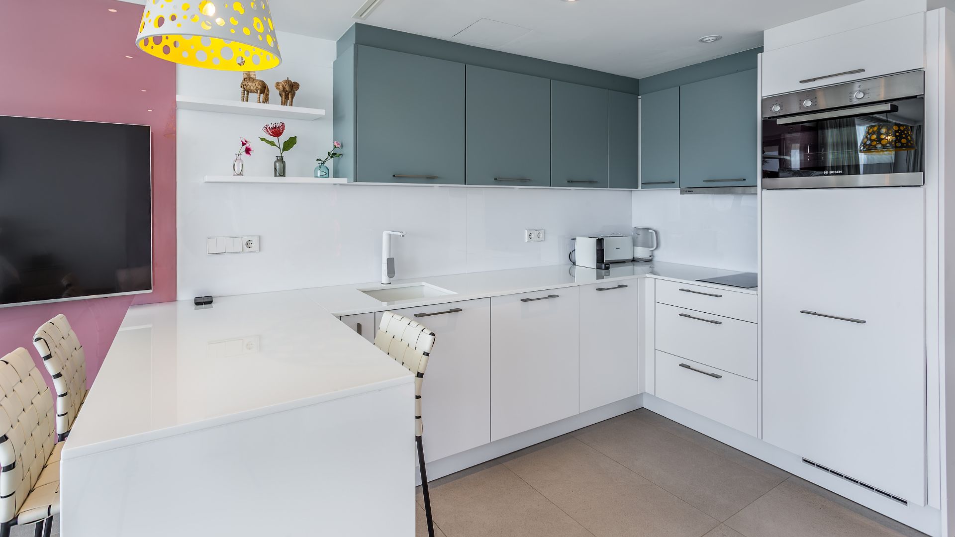 A modern kitchen with white cabinets, a Bosch oven, and a dining area with a white table and chairs.