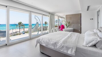 A modern hotel room with a large bed, a view of the beach, and a balcony with a hammock.