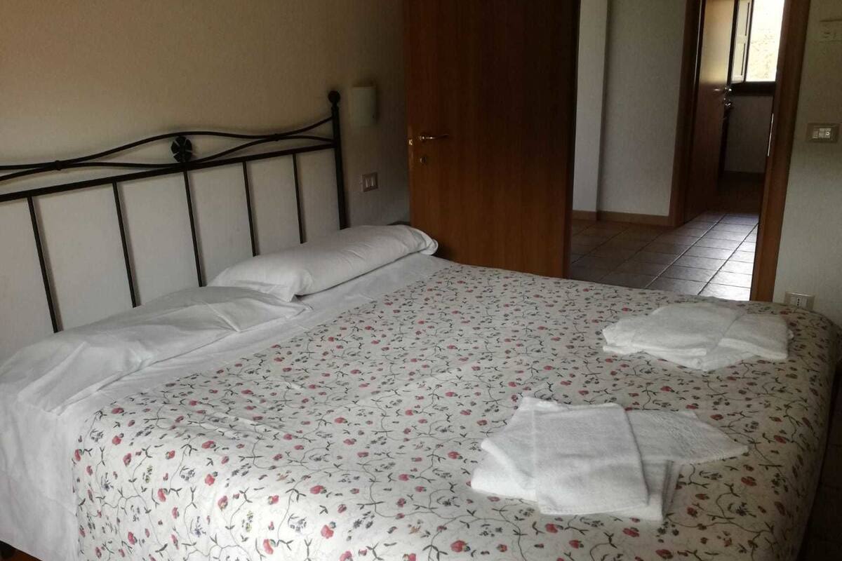 Een net opgemaakt bed met een bloemenbedekker en twee handdoeken erop.