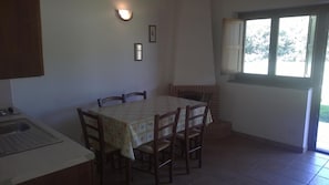 Un área de comedor con una mesa y sillas, una ventana con vistas, y una lámpara fijada a la pared.