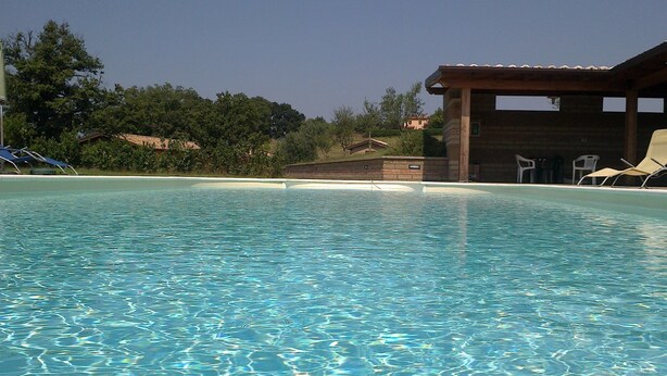 A clear swimming pool with lounge chairs and a wooden building in the background. - Agriturismo Monte dell'Olmo (Trevignano Romano)