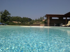 Una piscina cristalina con sillas de descanso y un edificio de madera al fondo.