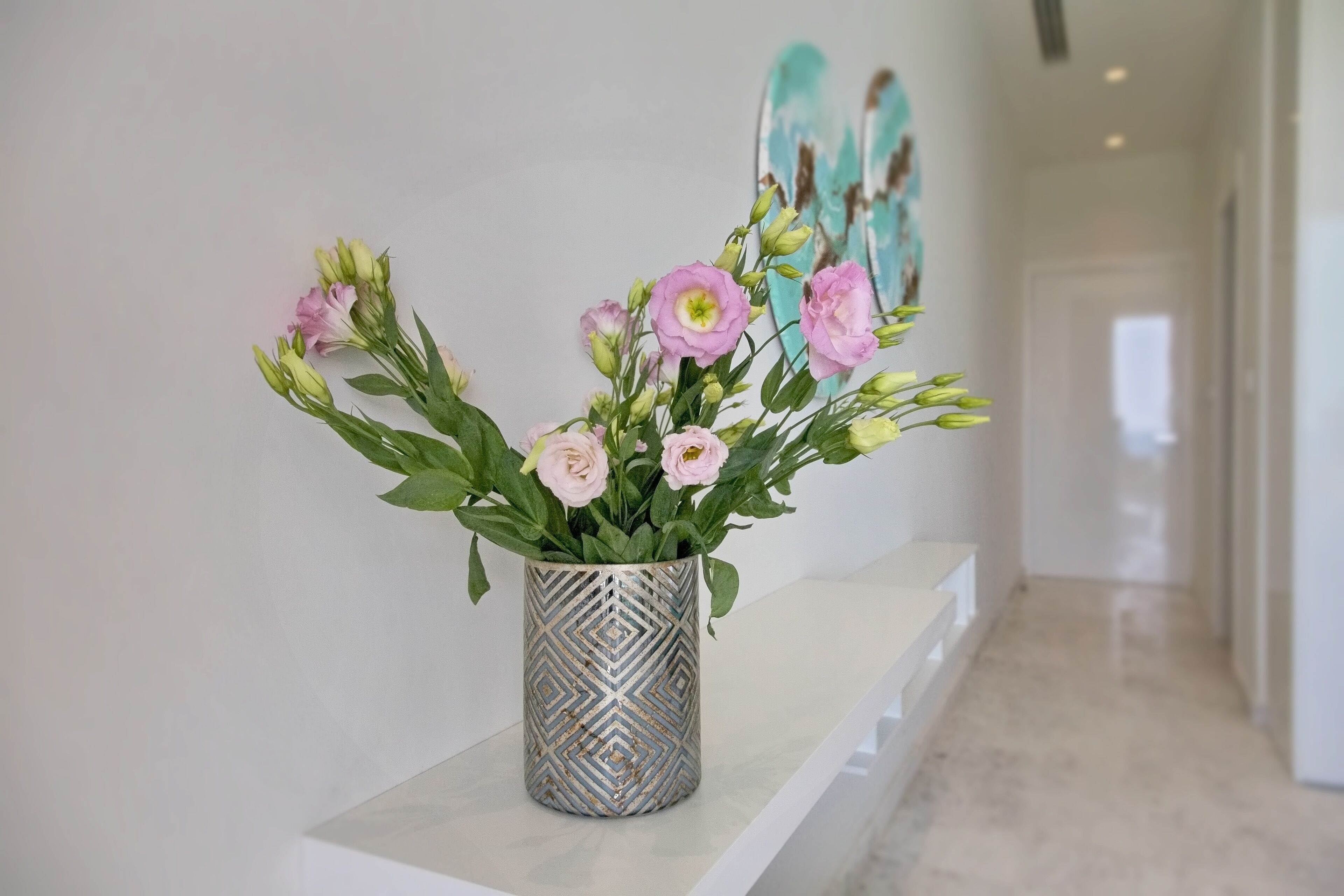 Un couloir avec un banc blanc et un vase rempli de fleurs roses.
