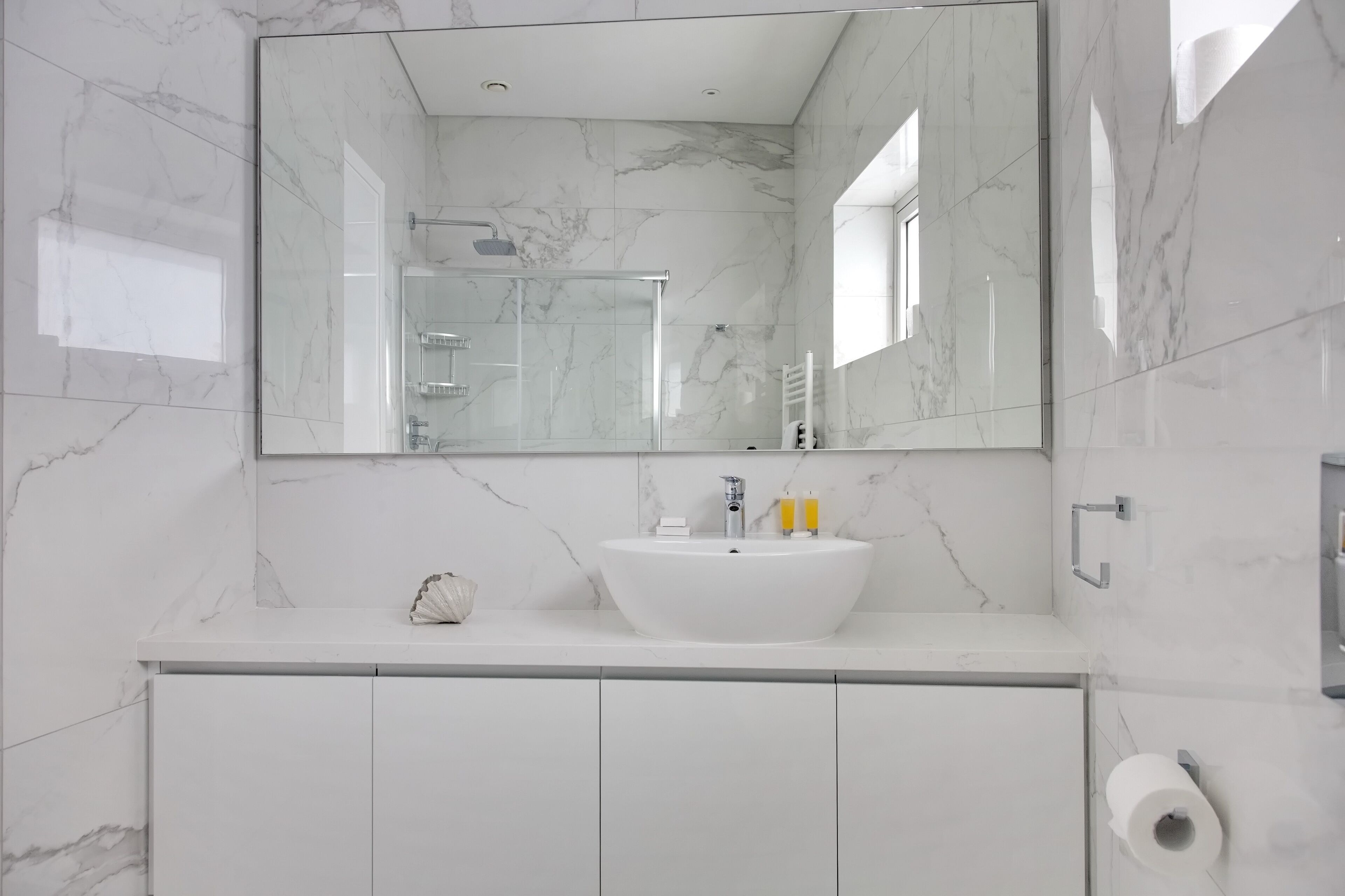A modern bathroom with a white marble sink, a large mirror, and a glass shower enclosure.