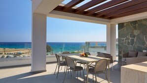 A modern outdoor dining area with a view of the ocean, a stone wall, and a wooden pergola. - Pearl Beachfront Villa (Ayia Napa)