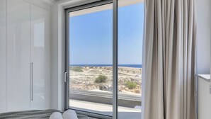 A bedroom with a large sliding glass door leading to a balcony with a view of rocky terrain and the sea. - Pearl Beachfront Villa (Ayia Napa)