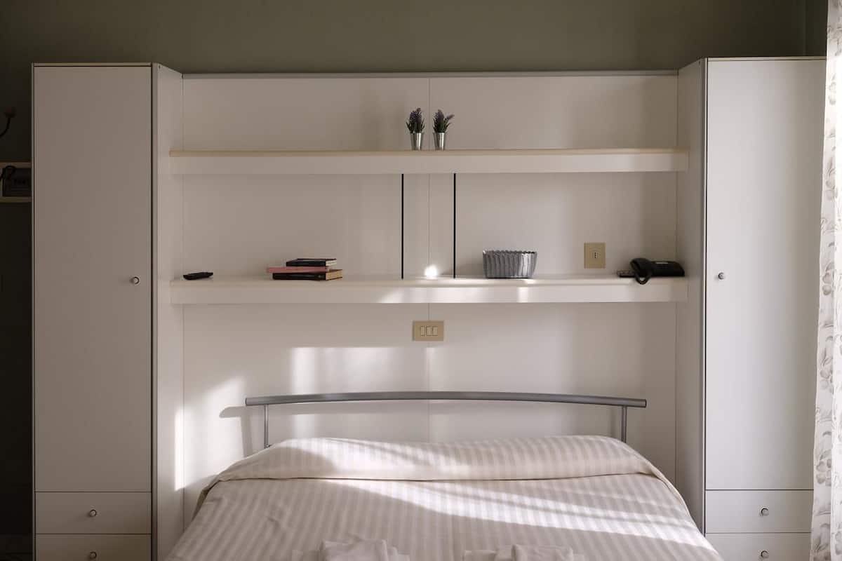 Un dormitorio con una cama, un armario y una estantería con libros y una planta.