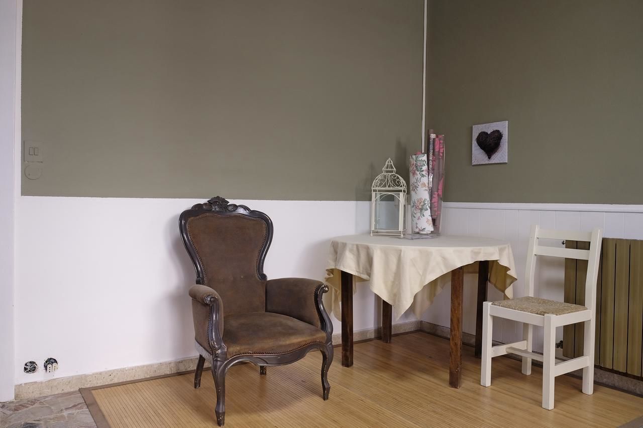 Een hoekkamer met een bruine gestoffeerde fauteuil, een witte stoel, een tafel met een witte tafelkleed, een witte lantaarn en een hartvormige decoratie aan de muur.