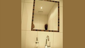 Une salle de bain avec un lavabo blanc, un robinet chromé et un miroir dont le cadre est orné de carreaux bruns.