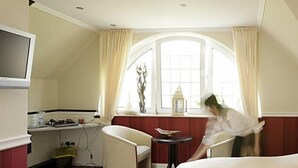 Une chambre d’hôtel comprenant un lit, un bureau avec un ordinateur, une chaise, une fenêtre avec des rideaux et une petite table avec une lampe.