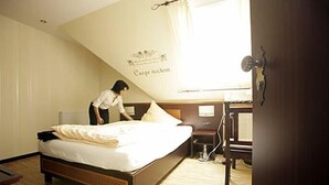 Une chambre à coucher comprenant un lit, une table de chevet, une commode, une fenêtre avec des rideaux et un mur orné d’un panneau décoratif.
