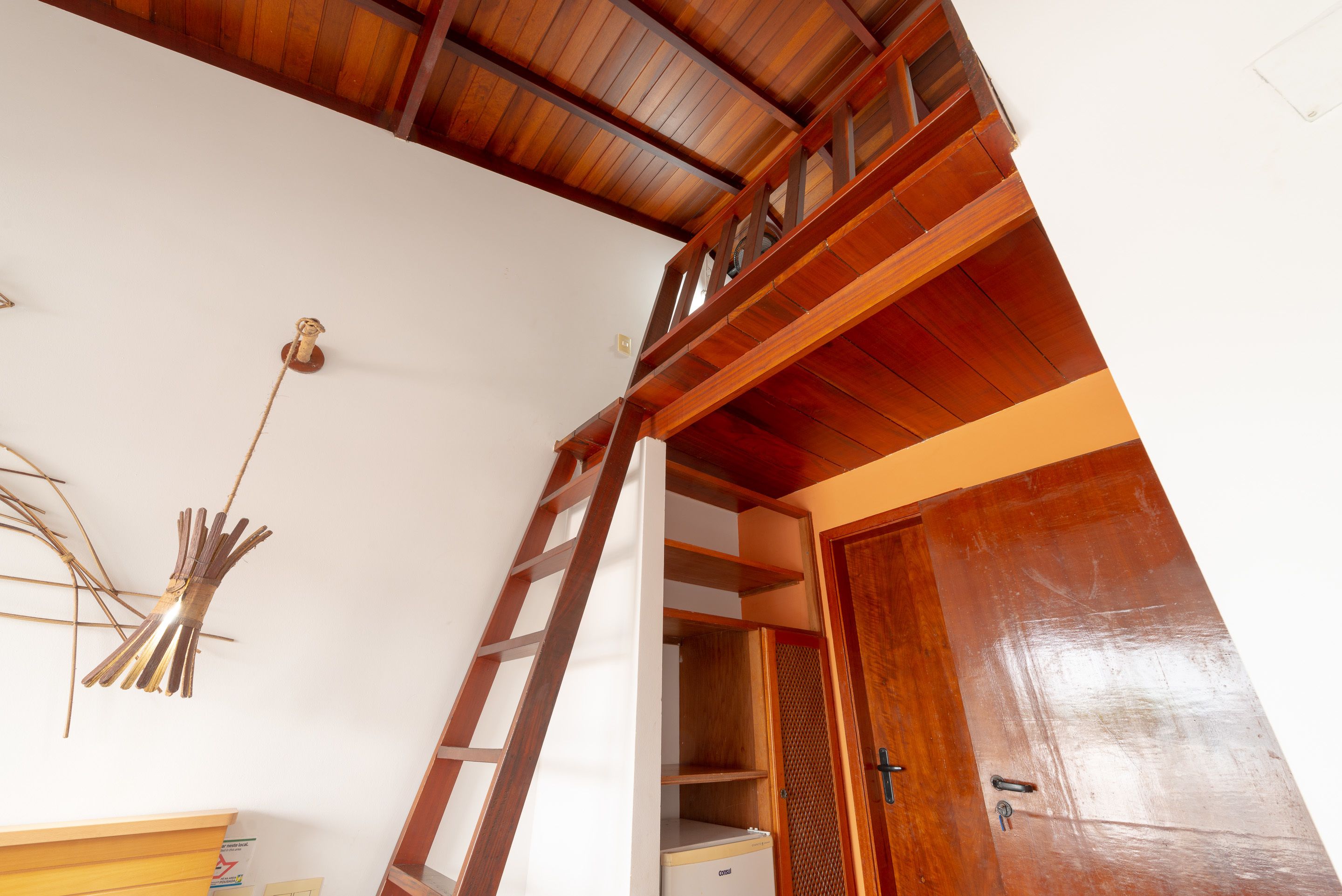 Uma escada de madeira leva a um espaço de loft com uma escada, uma parede branca e uma porta de madeira.