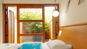 Ein Schlafzimmer mit einem Bett, einem Fenster mit Holzjalousien, einem Nachttisch und einer Pendelleuchte.