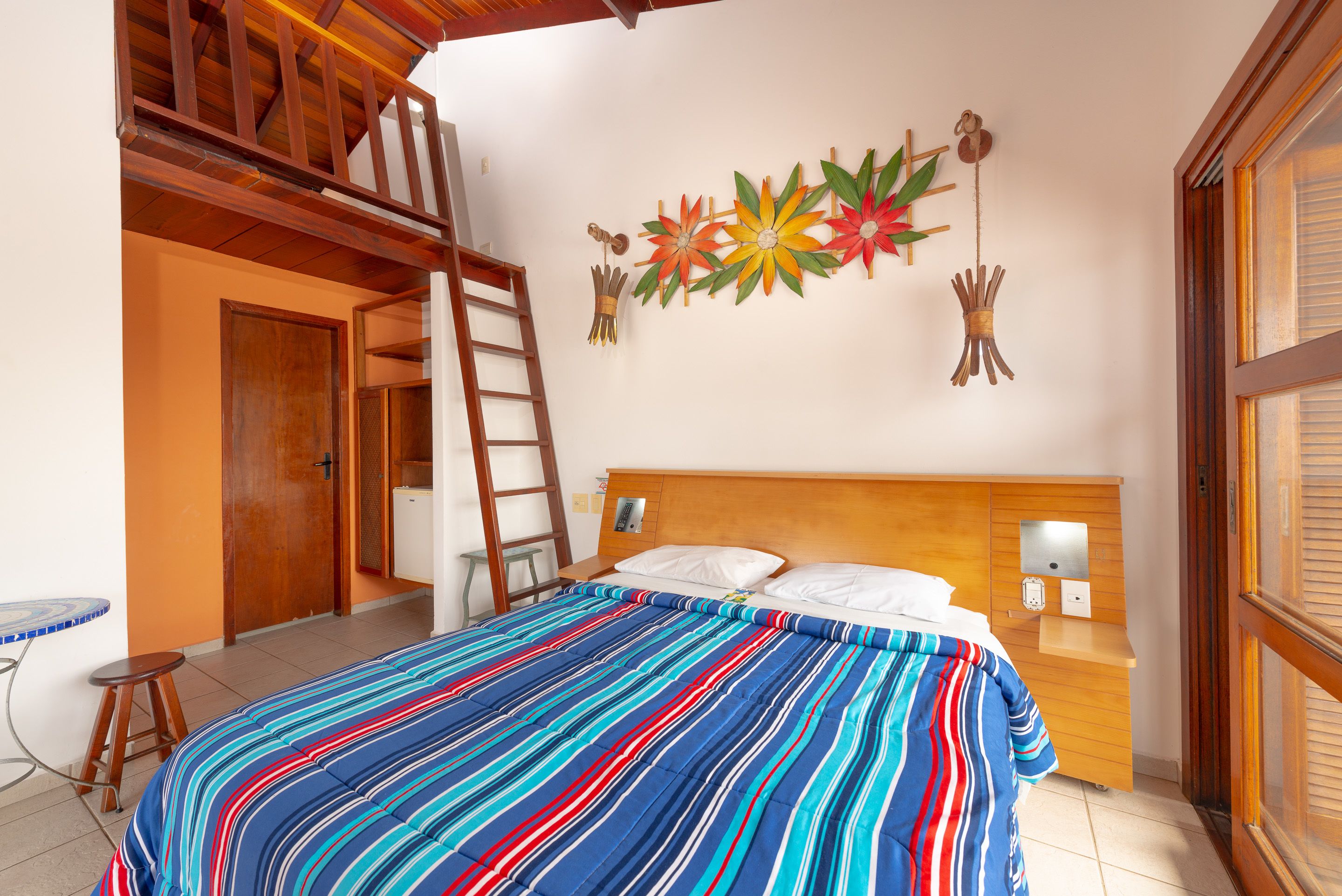 Een slaapkamer met een bed, houten hoofdbord, een ladder, een muur met decoratieve details en een raam.