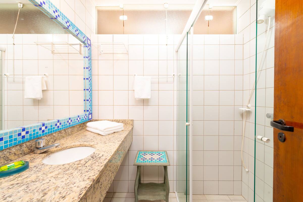 Ein Badezimmer mit Marmorwaschbecken, einer kleinen Hocker, einer Duschkabine aus Glas und einer Holztür.
